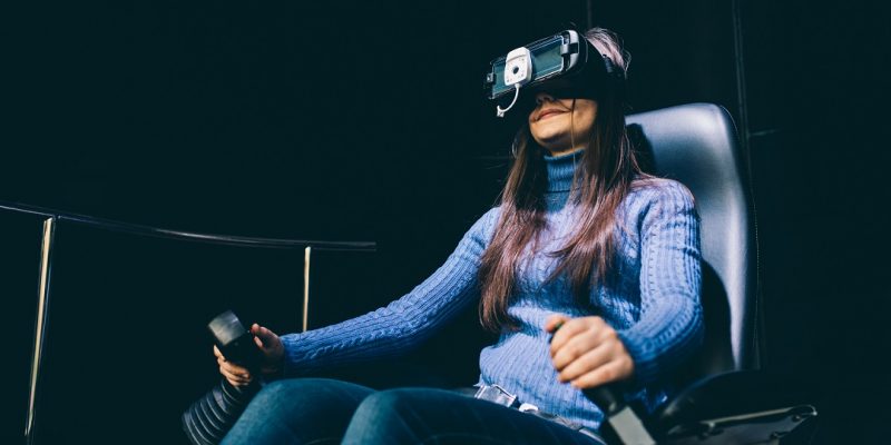 Young beautiful eastern woman sitting on a gaming chair testing augmented reality with 3D viewer - games, futuristic, augmented reality concept